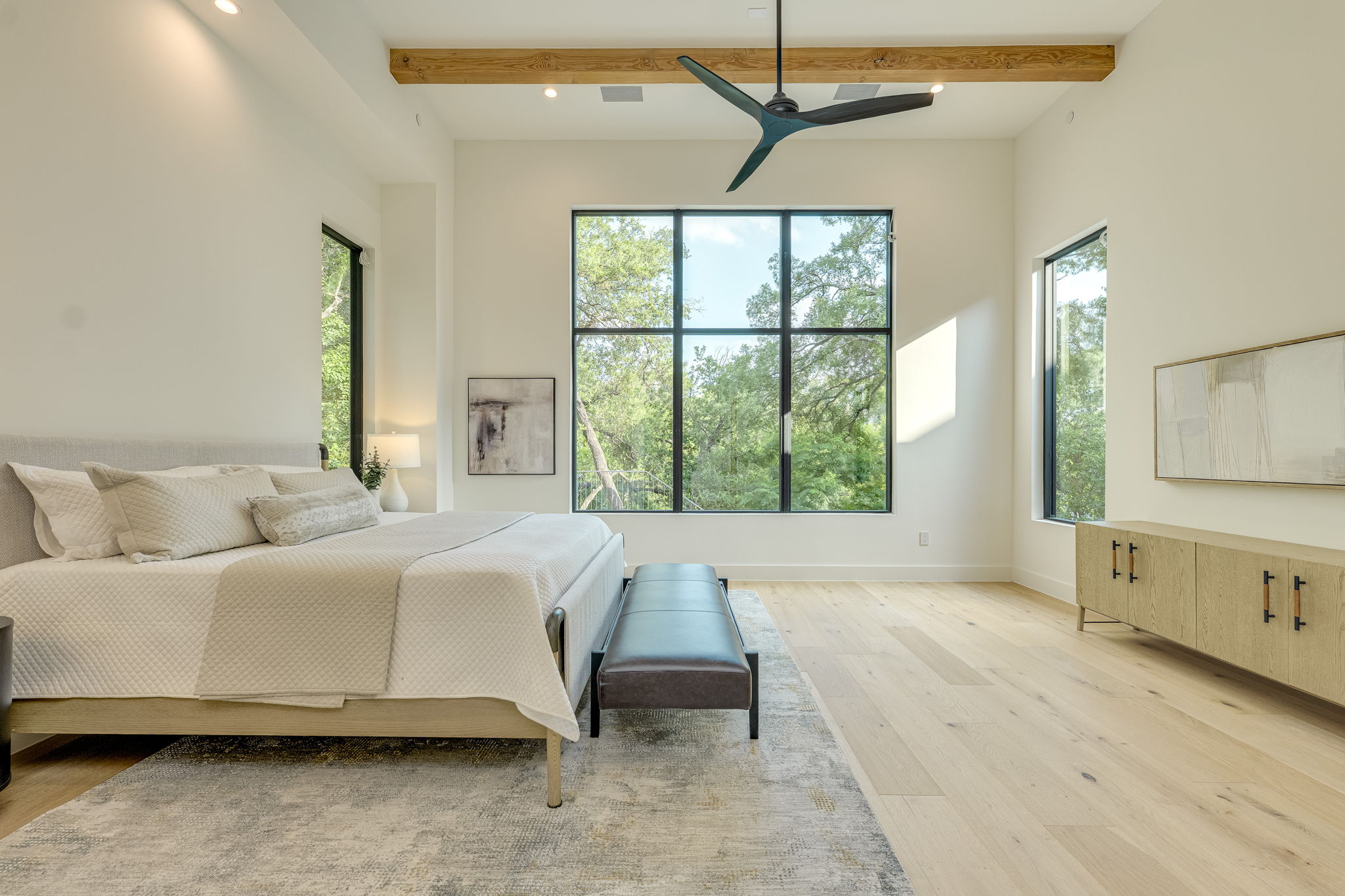 405 Honeycomb Ridge Austin, TX 78746 - Photo 9 of 15 Tree-lined views fill this airy bedroom, showcasing high ceilings with an exposed beam and a modern ceiling fan.