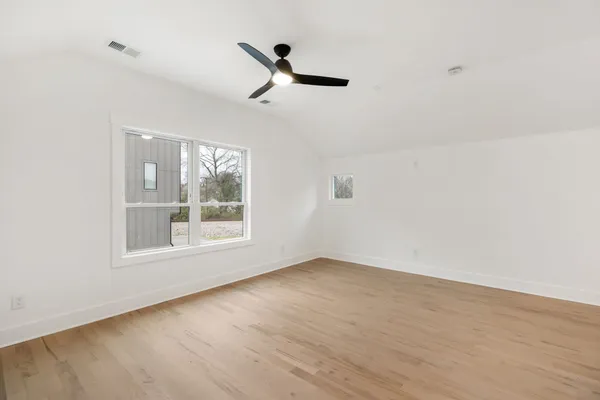 an empty room with wooden floor ceiling fan and windows
