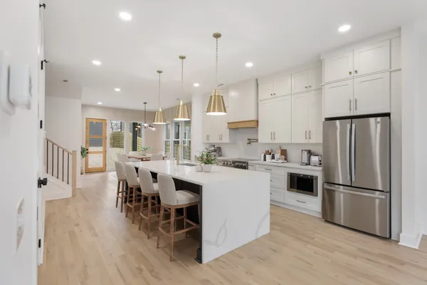 a kitchen with stainless steel appliances kitchen island granite countertop a refrigerator a stove a sink a dining table and chairs with wooden floor