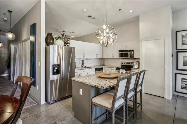 a kitchen with stainless steel appliances granite countertop a dining table chairs refrigerator and microwave