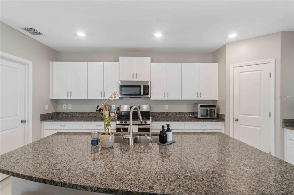 9440 Lemon Drop Loop Sun City Center, FL 33573 - Photo 12 of 55 a kitchen with kitchen island granite countertop a sink a stove counter space and cabinets