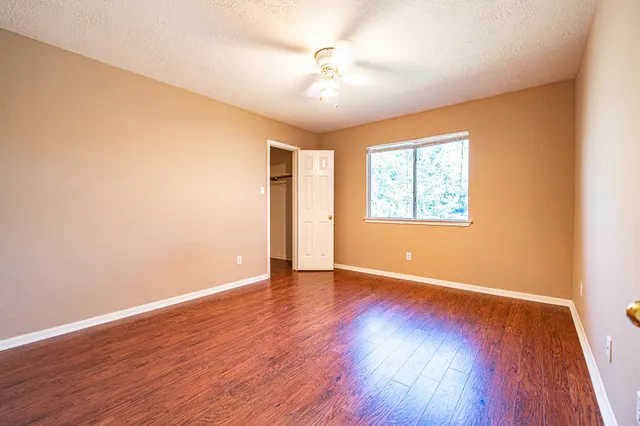 an empty room with wooden floor chandelier fan and windows