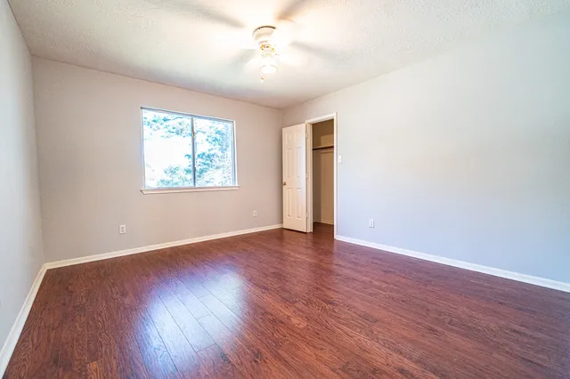 an empty room with wooden floor ceiling fan and windows