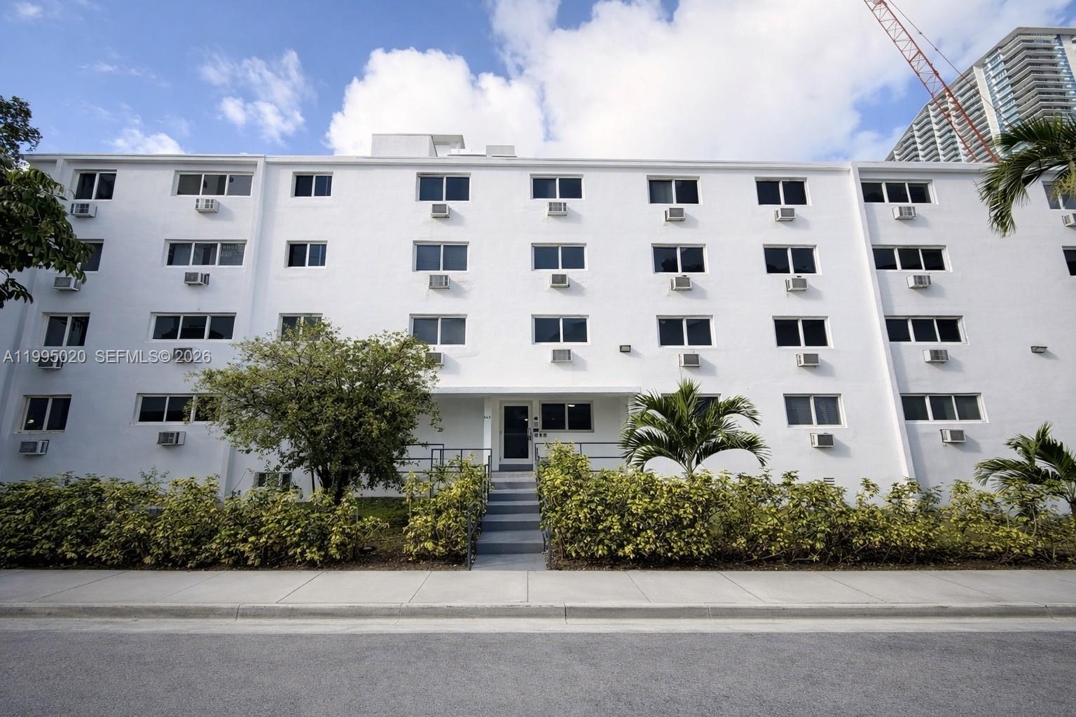 a front view of a multi story building with yard and parking space