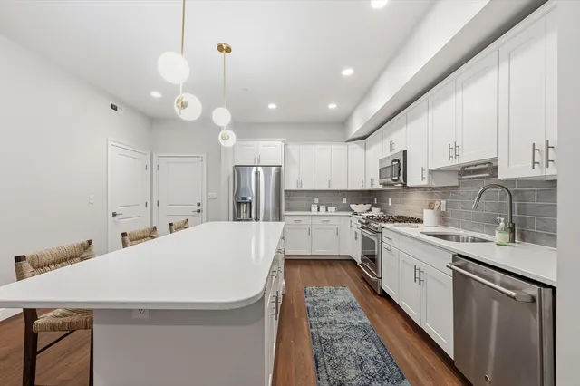 a open kitchen with stainless steel appliances granite countertop a sink a stove a refrigerator and white cabinets with wooden floor