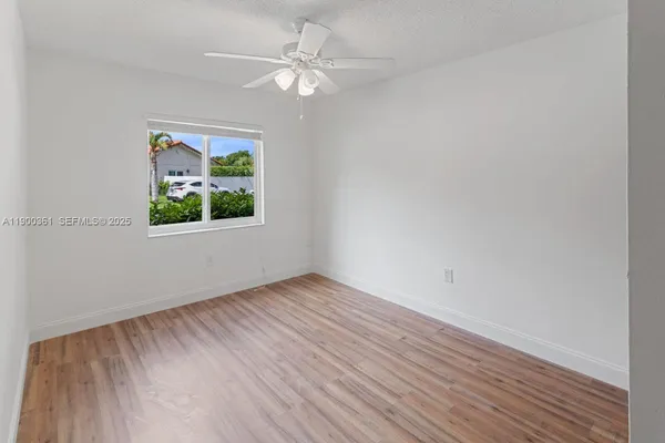 an empty room with wooden floor chandelier fan and windows