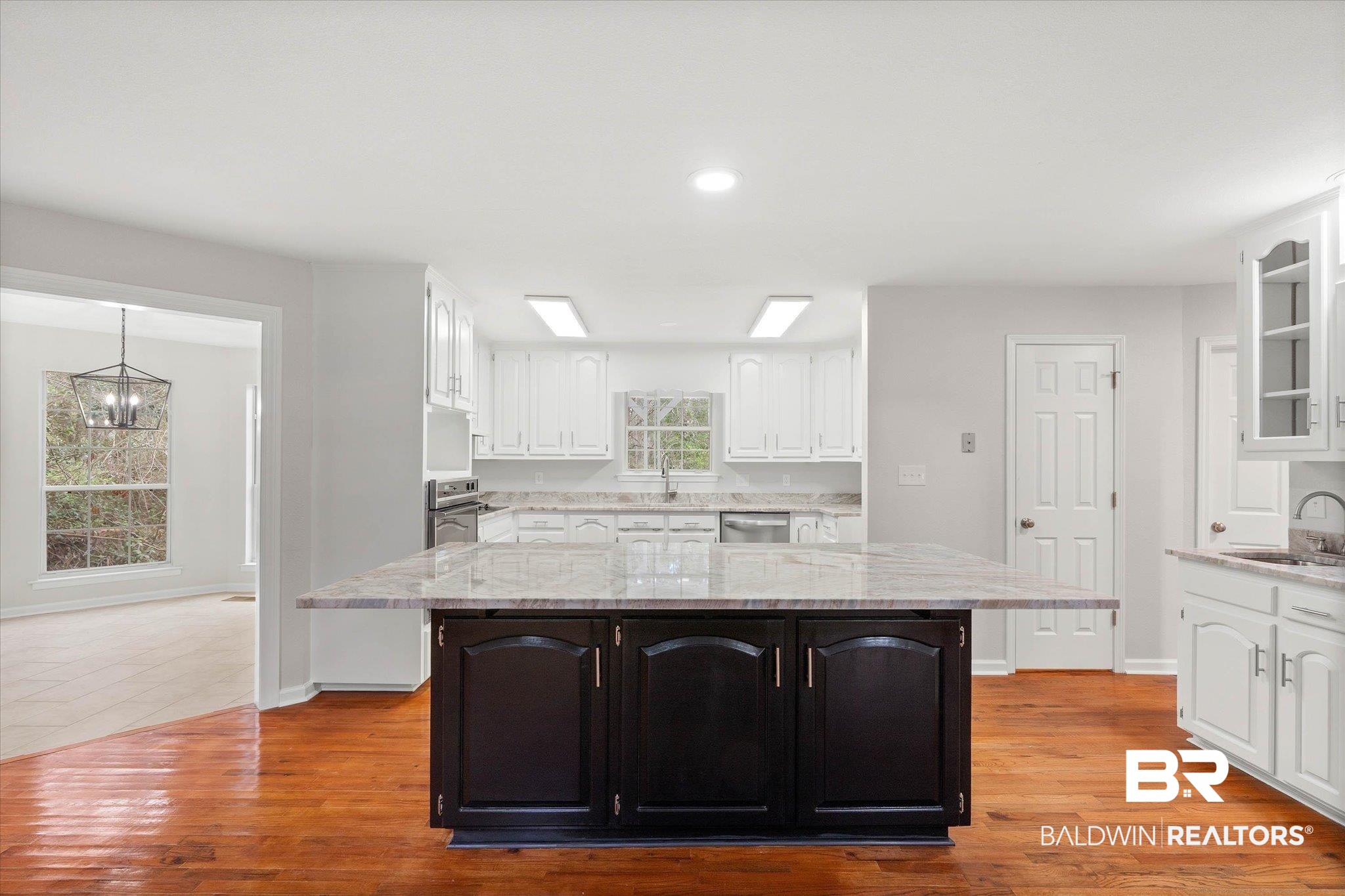 106 Melanie Loop Daphne, AL 36526 - Photo 8 of 45 Dual tone kitchen featuring dual tone cabinets, light stone countertops, a center island, light wood-style flooring, and hanging lights