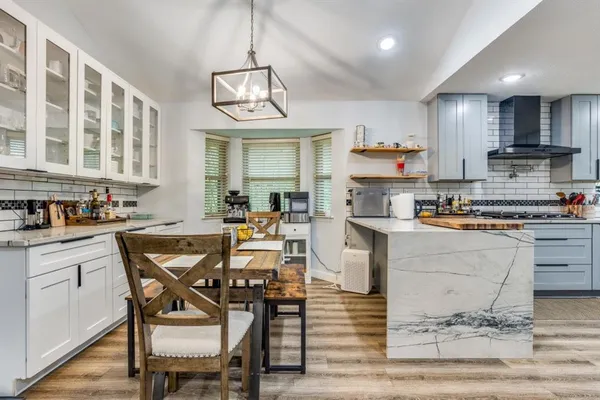 a kitchen with stainless steel appliances granite countertop a stove top oven a sink a dining table and chairs with wooden floor