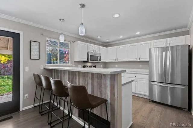 a kitchen with stainless steel appliances granite countertop a refrigerator a sink dishwasher a stove and a dining table with wooden floor