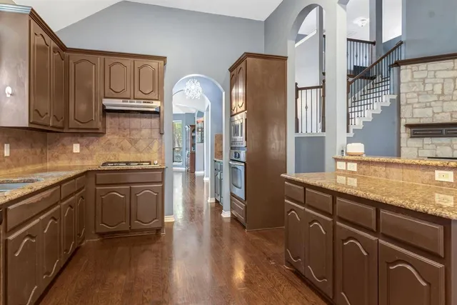 a kitchen with stainless steel appliances granite countertop a refrigerator a sink dishwasher and wooden cabinets with wooden floor