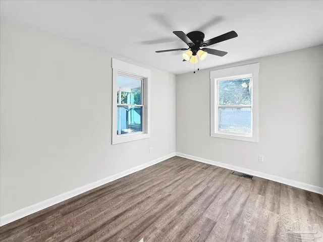 an empty room with wooden floor ceiling fan and windows