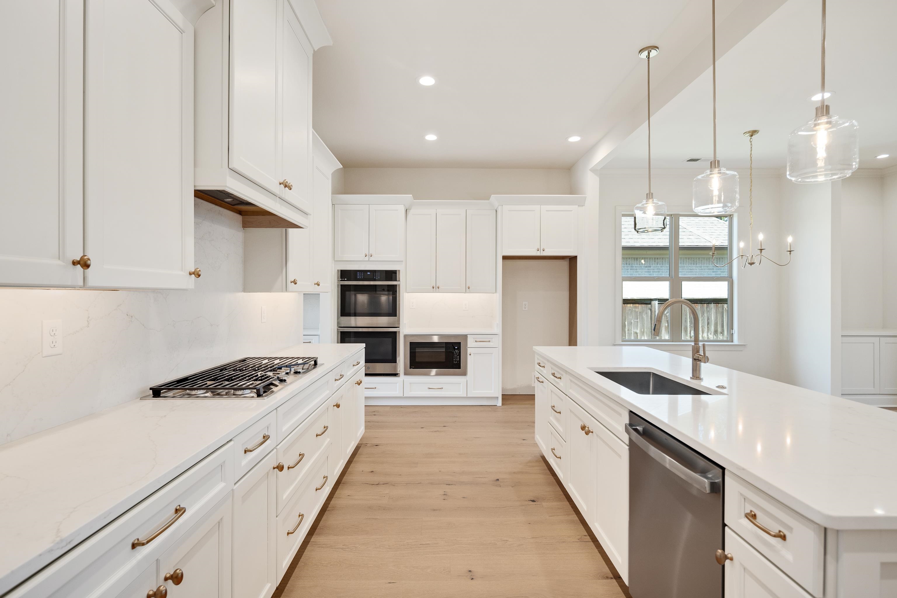 3406 Village Cross Loop Collierville, TN 38017 - Photo 9 of 40 White shaker cabinetry with brass hardware, light wood-finish flooring, integrated stainless steel appliances, recessed lighting, and a kitchen island with an undermount sink