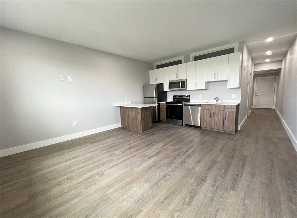 80 Bridge Street, Unit 303 Dedham, MA 02026 - Photo 10 of 18 a large kitchen with a wooden floor and stainless steel appliances