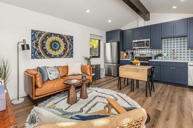 a living room with stainless steel appliances furniture a rug and a kitchen view