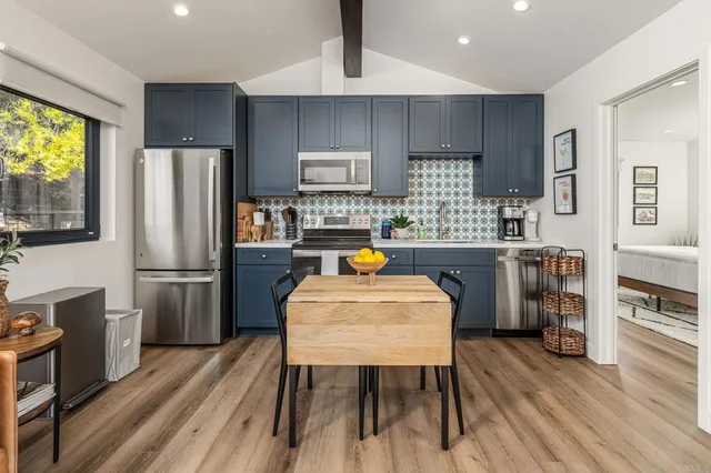 a kitchen with stainless steel appliances a refrigerator a stove a sink a dining table and chairs with wooden floor