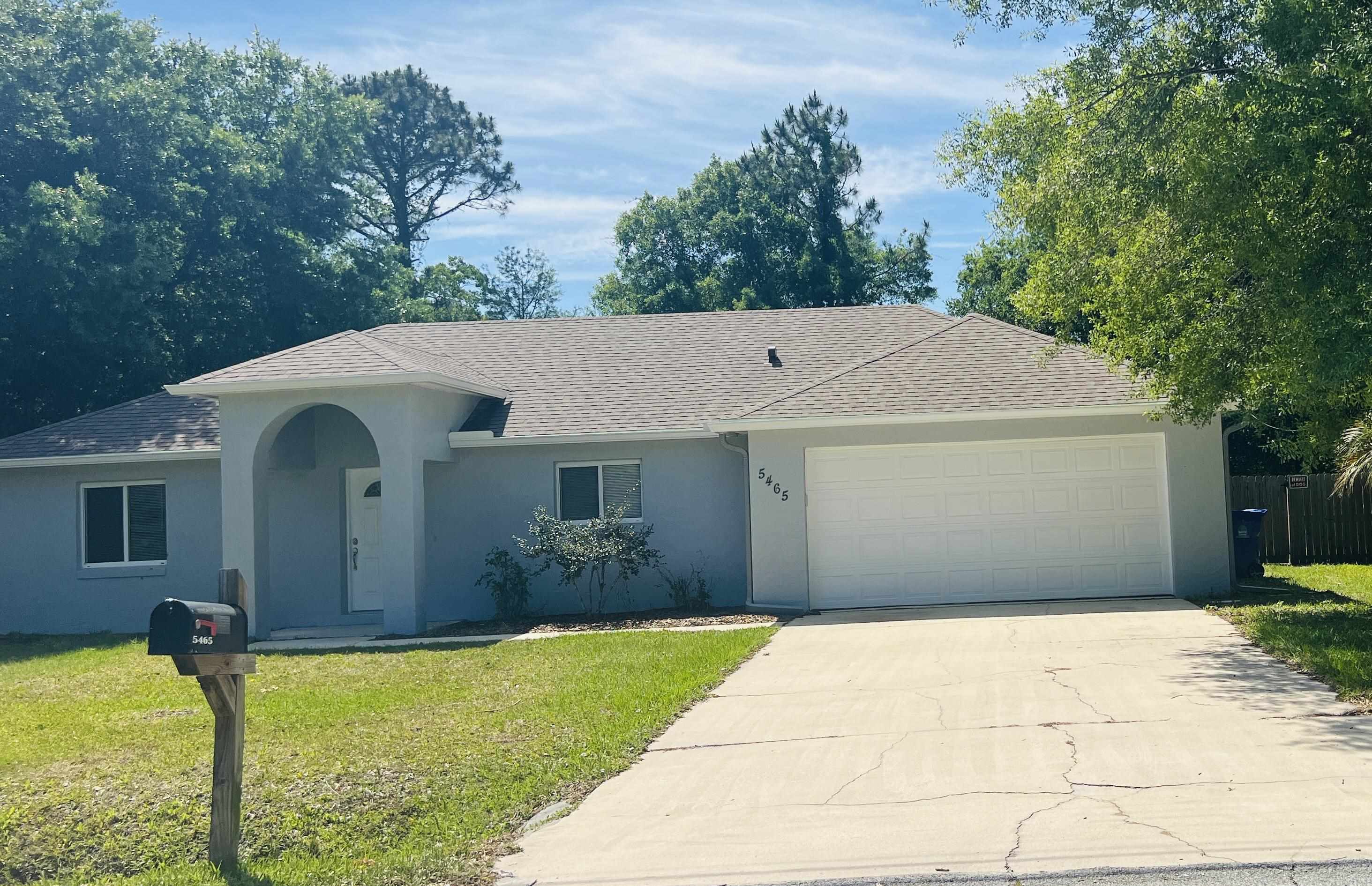a view of a white house with a yard plants and large tree