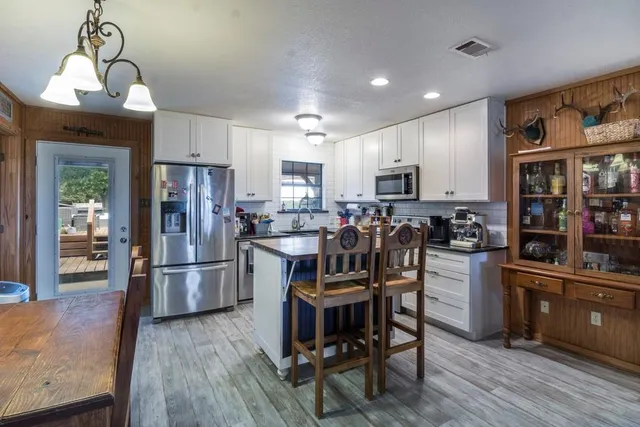 a kitchen with stainless steel appliances kitchen island granite countertop a refrigerator a stove a sink a dining table and chairs with wooden floor