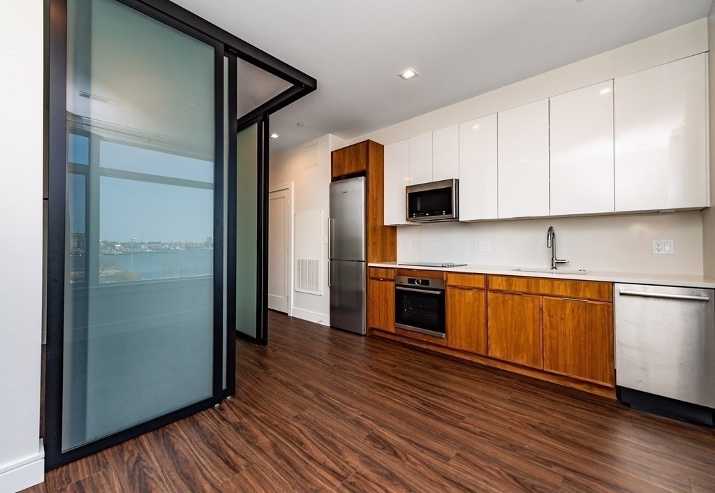 99 Sumner Street, Unit 413 Boston, MA 02128 - Photo 3 of 17 a kitchen with stainless steel appliances granite countertop a refrigerator a sink and white cabinets with wooden floor