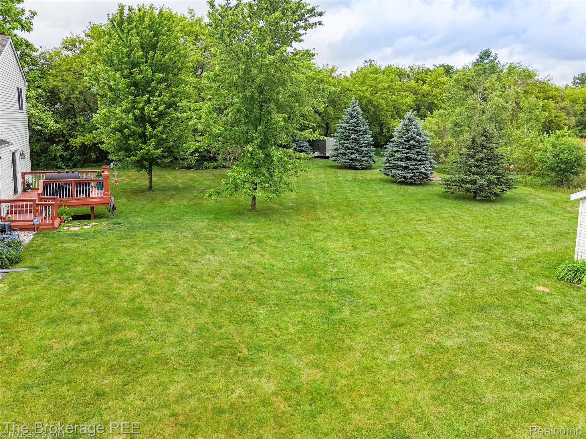 4432 North Belsay Road Flint, MI 48506 - Photo 15 of 79 Expansive green lawn with mature trees, a wooden deck, and a white storage shed