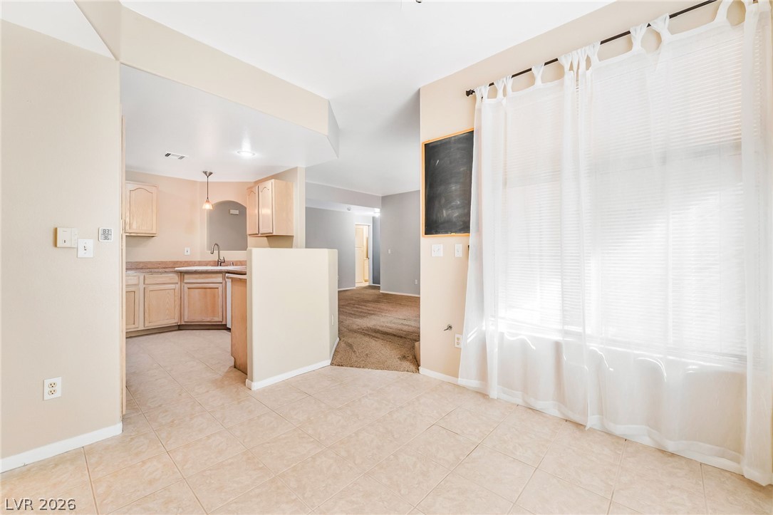 2050 West Warm Springs Road, Unit 2411 Henderson, NV 89014 - Photo 11 of 37 A well-lit kitchen area, featuring warm-toned cabinetry and a tiled floor, opens into a carpeted adjacent room.