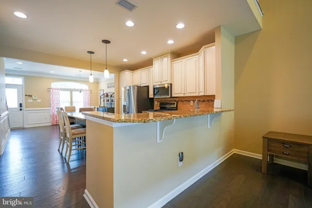 a kitchen with stainless steel appliances a refrigerator a stove a sink dishwasher with a dining table and chairs with wooden floor