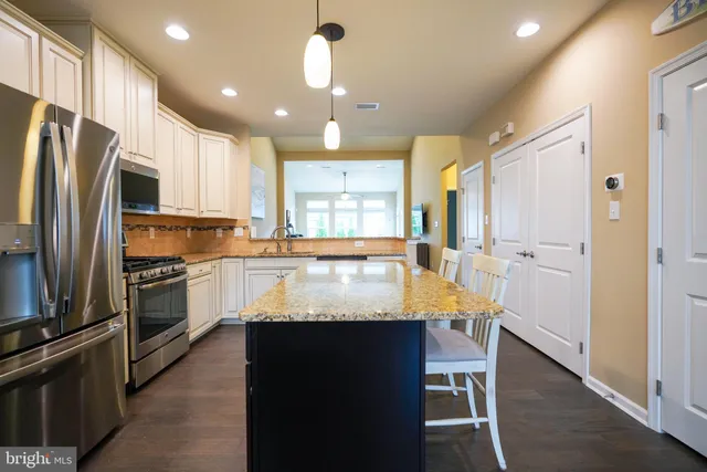 a large kitchen with kitchen island granite countertop a refrigerator a stove a sink a dining table and chairs with wooden floor