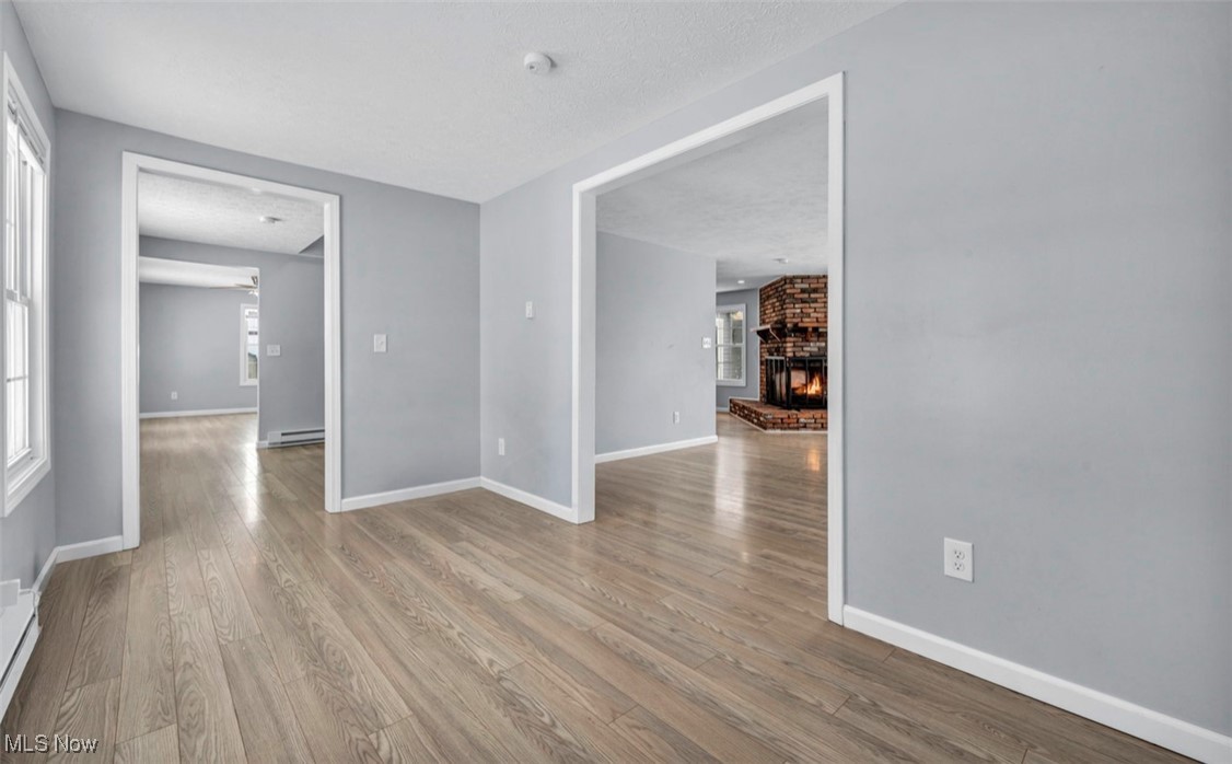 3961 Dayton Road Madison, OH 44057 - Photo 15 of 36 Spare room with baseboard heating, light hardwood / wood-style flooring, a wealth of natural light, and a fireplace