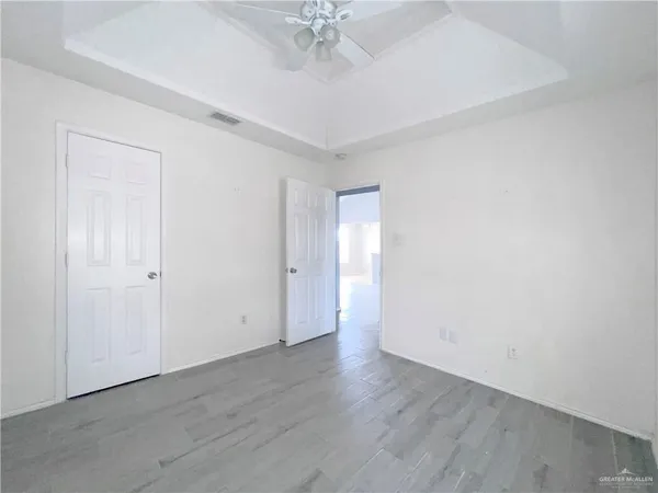 an empty room with a chandelier fan and wooden floor