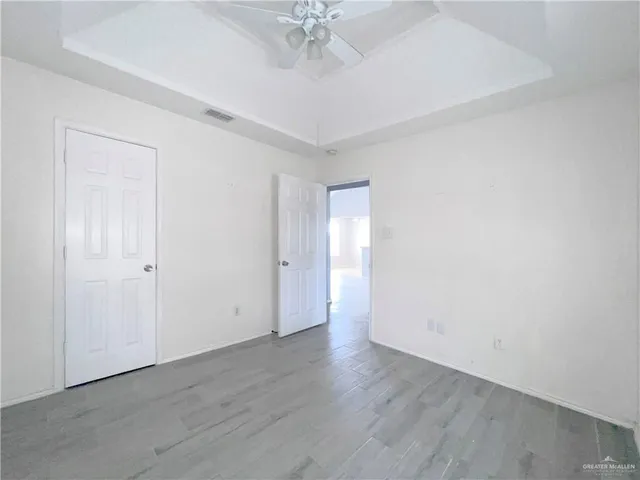 an empty room with a chandelier fan and wooden floor