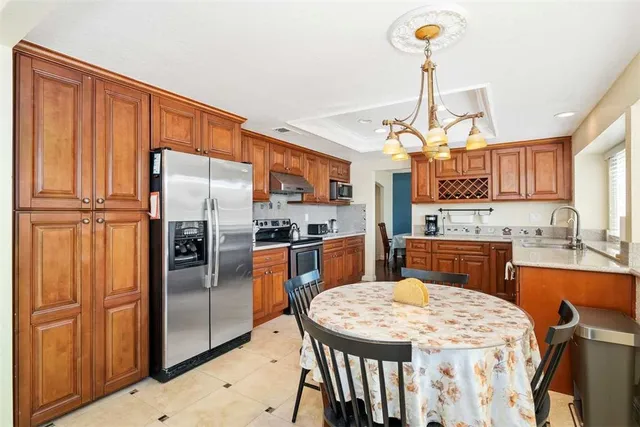 a kitchen with stainless steel appliances granite countertop a refrigerator a sink dishwasher a stove and a dining table with wooden floor