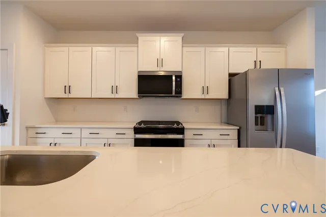 a kitchen with stainless steel appliances a refrigerator a stove top oven a sink and white cabinets