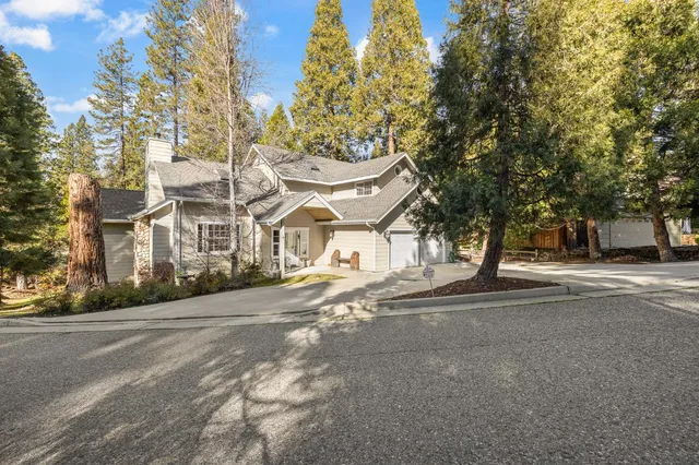a view of a white house next to a road with large trees