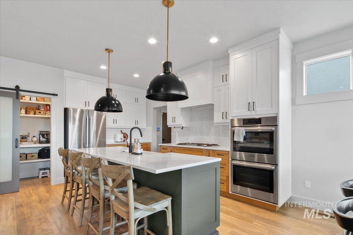 4150 East Fratello Street Meridian, ID 83642 - Photo 11 of 46 Kitchen with a barn door, appliances with stainless steel finishes, white cabinetry, tasteful backsplash, and decorative light fixtures