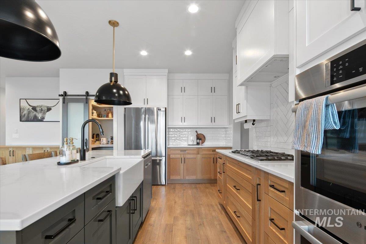 4150 East Fratello Street Meridian, ID 83642 - Photo 12 of 46 Kitchen featuring a barn door, appliances with stainless steel finishes, tasteful backsplash, a center island with sink, and light wood finished floors