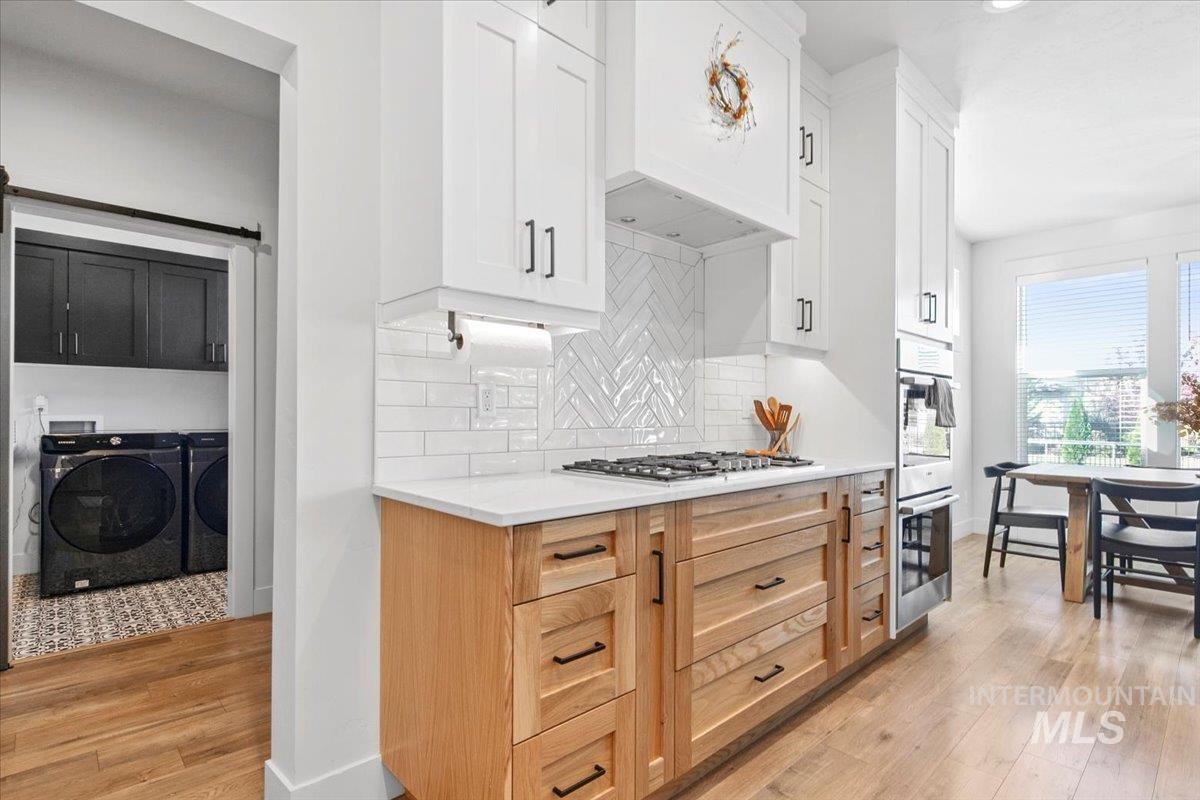 4150 East Fratello Street Meridian, ID 83642 - Photo 16 of 46 Kitchen with light wood-style flooring, independent washer and dryer, premium range hood, and white cabinets