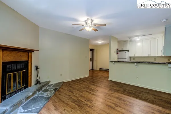 a view of an empty room and kitchen with wooden floor