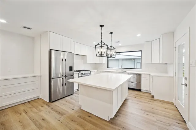 a kitchen with stainless steel appliances a stove a refrigerator and white cabinets with wooden floor