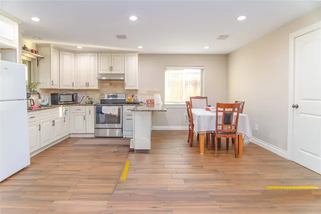 a kitchen with stainless steel appliances granite countertop a stove top oven a sink dishwasher and white cabinets with wooden floor