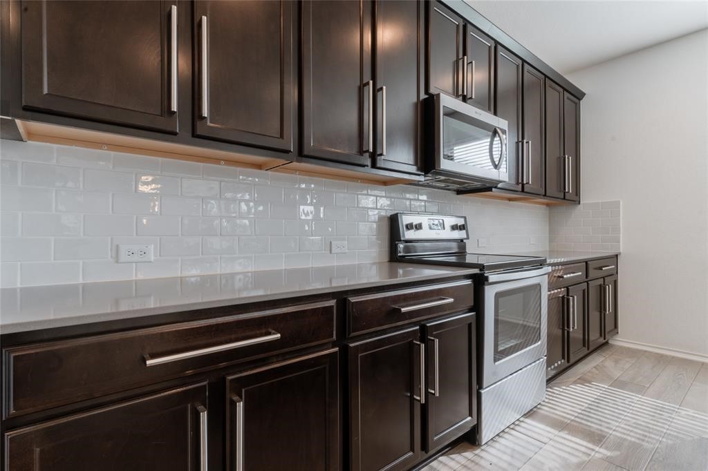 1333 Terrace View Drive Georgetown, TX 78628 - Photo 14 of 35 Modern kitchen with dark wood cabinetry, white subway tile backsplash, and sleek appliances.