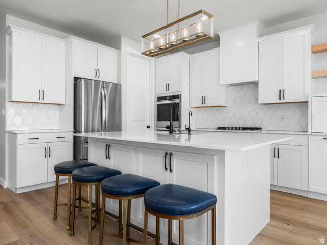 2786 West Hancock Street, Unit 198 Mapleton, UT 84664 - Photo 7 of 33 Modern kitchen featuring an expansive center island with seating, white shaker cabinetry, stainless steel appliances, and wood-finish flooring