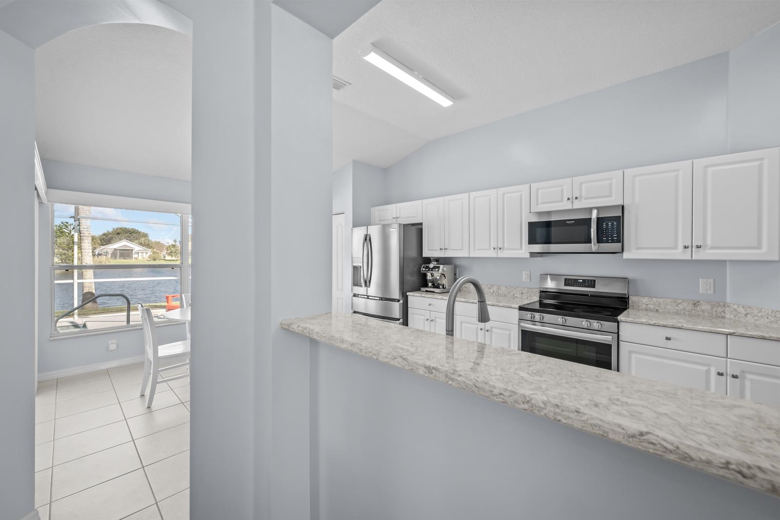1116 Compass Row St. Augustine, FL 32080 - Photo 15 of 68 Kitchen with white cabinets, appliances with stainless steel finishes, light stone countertops, light tile patterned floors, and vaulted ceiling