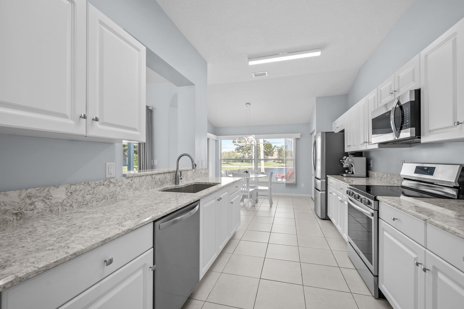 1116 Compass Row St. Augustine, FL 32080 - Photo 17 of 68 Kitchen featuring stainless steel appliances, vaulted ceiling, white cabinets, light stone countertops, and light tile patterned floors
