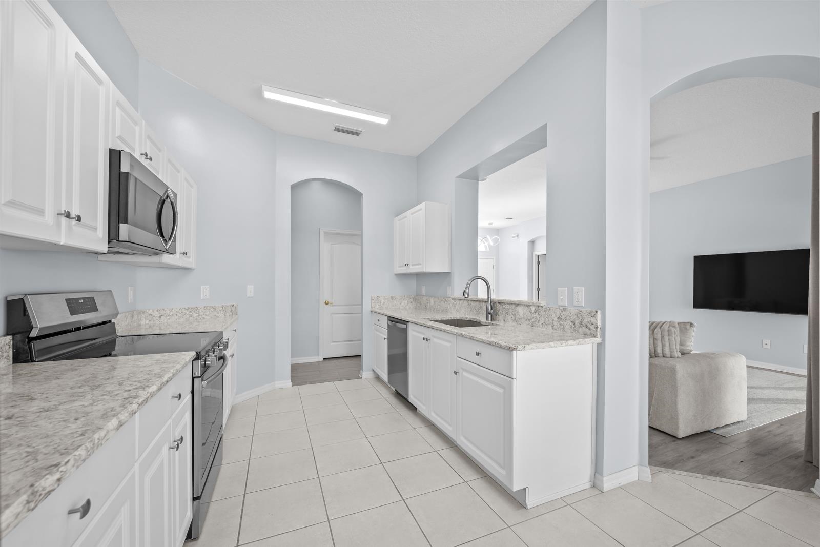 1116 Compass Row St. Augustine, FL 32080 - Photo 19 of 68 Kitchen with arched walkways, appliances with stainless steel finishes, white cabinets, light stone countertops, and light tile patterned floors