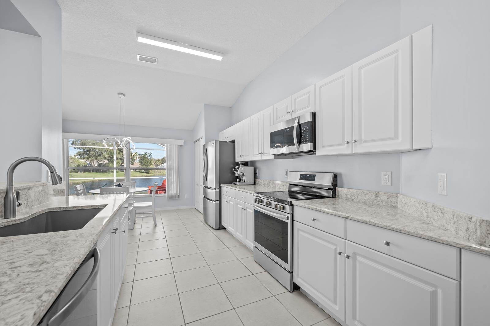 1116 Compass Row St. Augustine, FL 32080 - Photo 20 of 68 Kitchen featuring white cabinets, appliances with stainless steel finishes, light stone countertops, a water view, and lofted ceiling