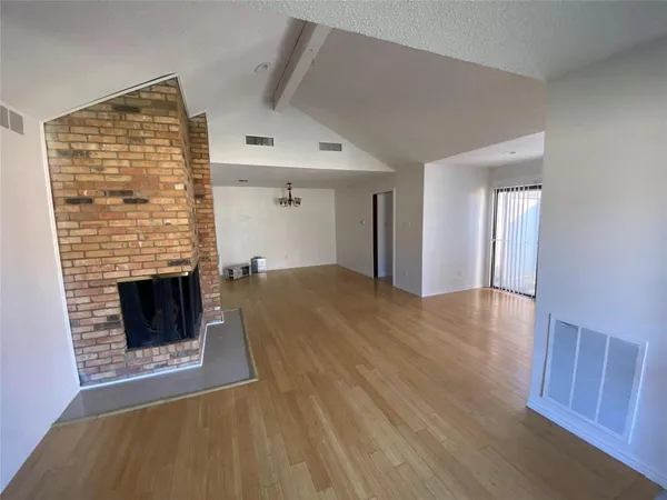 a view of an empty room with wooden floor fireplace and a window
