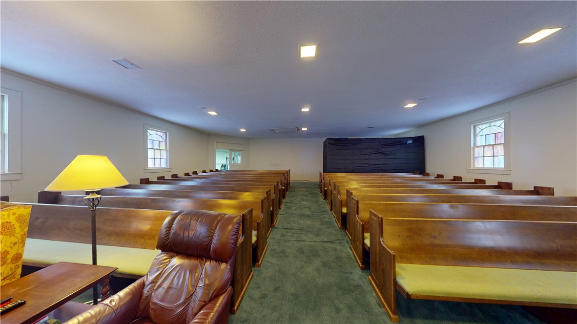 415 Church Street Pendleton, SC 29670 - Photo 14 of 35 A quiet assembly room features wooden pews, a carpeted aisle, and decorative windows.