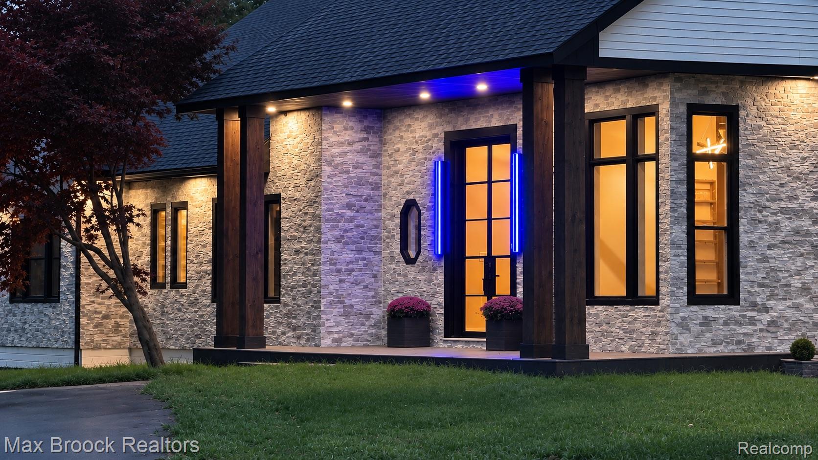 Stone veneer exterior with dark-framed windows, a prominent entry door, wood-wrapped structural columns, and a dark shingle roof