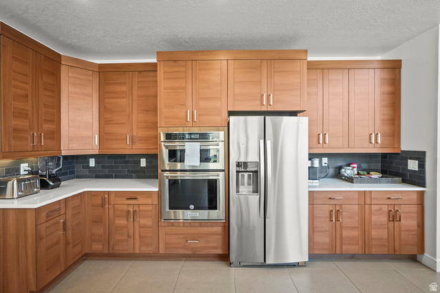 15008 South Springtime Road Draper, UT 84020 - Photo 11 of 37 Kitchen with stainless steel appliances, backsplash, a textured ceiling, and wood finish cabinets