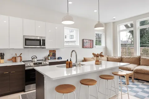 a kitchen with granite countertop a sink a stove a kitchen island with chairs and white cabinets