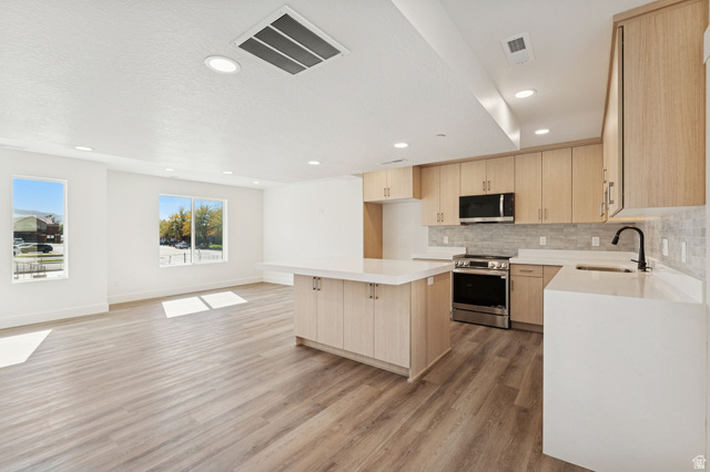 254 North Main Street Bountiful, UT 84010 - Photo 3 of 45 Kitchen featuring light brown cabinetry, a kitchen island, stainless steel appliances, decorative backsplash, and light wood finished floors
